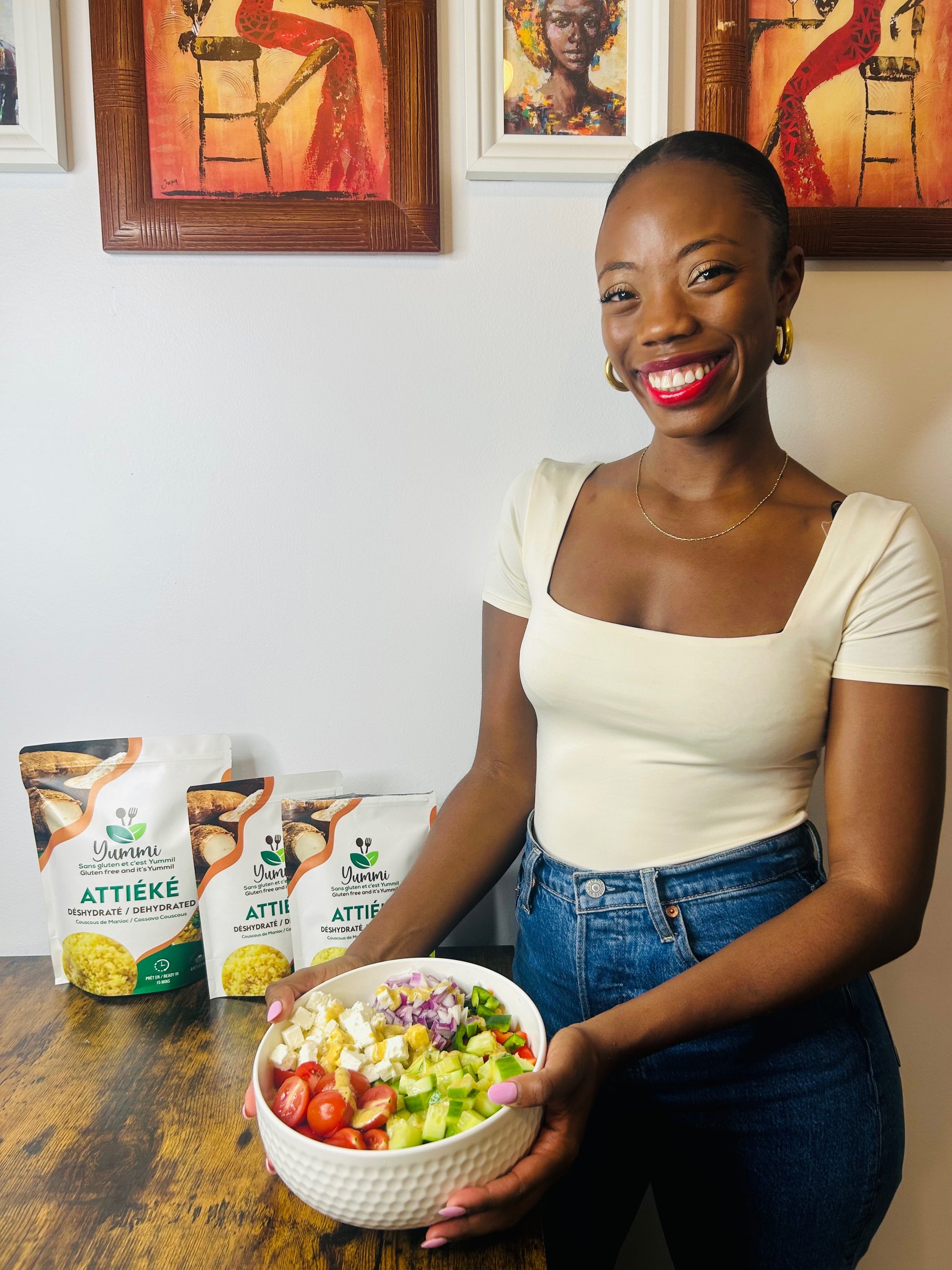 Femme souriante tenant une assiette d’attiéké en salade grecque, garnie de légumes frais comme des tomates, des concombres et de la feta. Un plat coloré et appétissant, parfait pour un repas léger.
